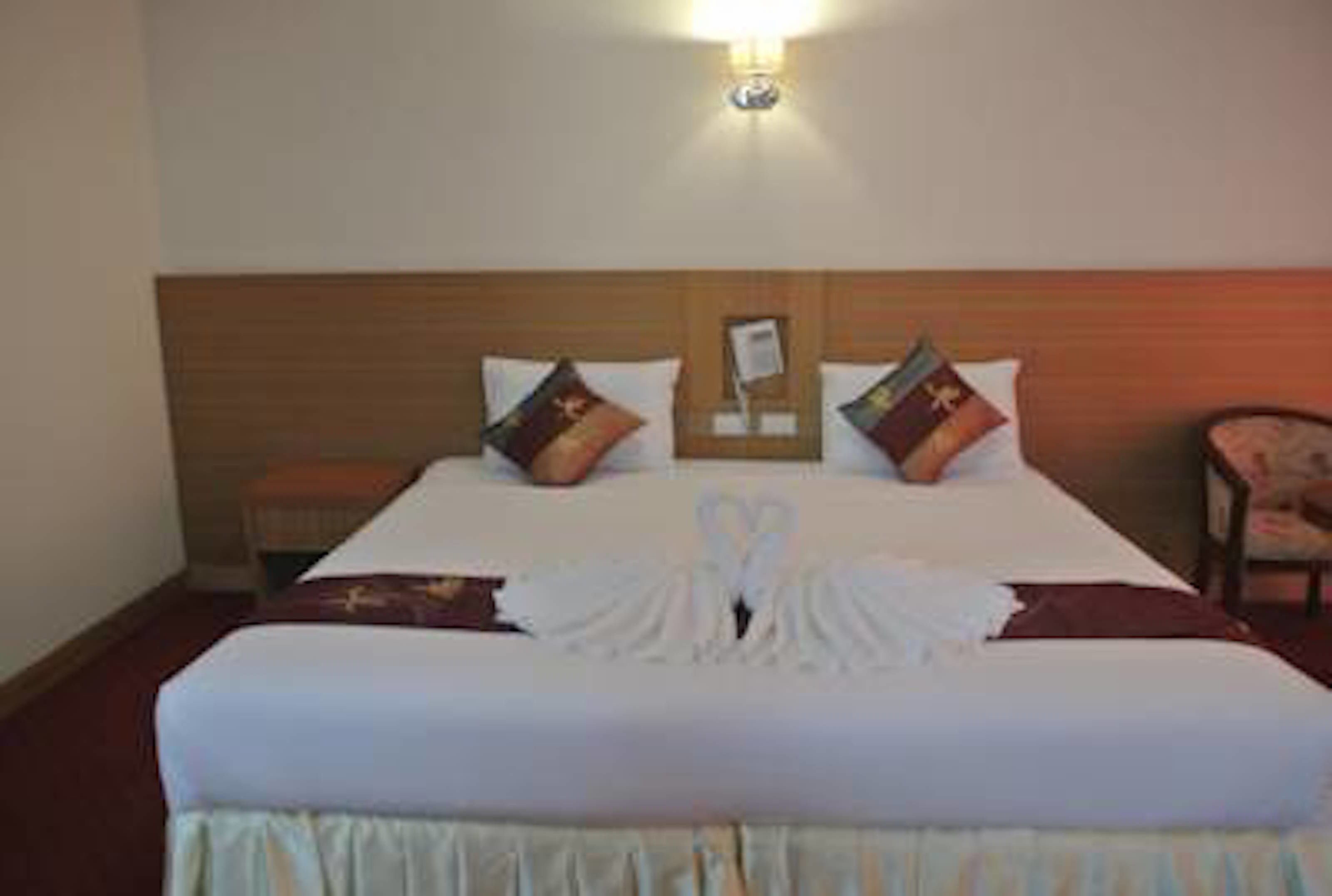 A hotel room with a neatly made bed, a bedside table, and a wall-mounted lamp.