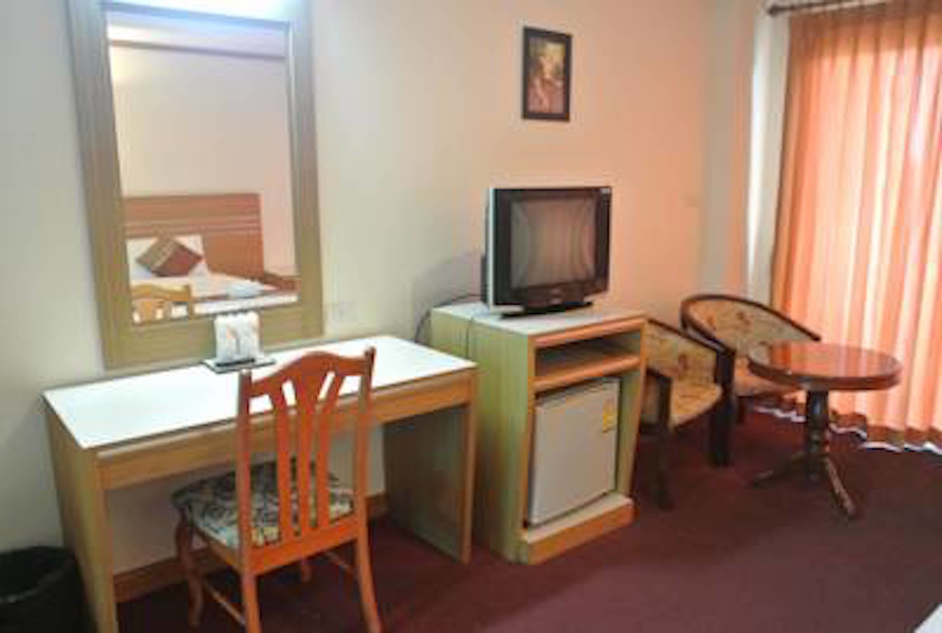 Ein kompaktes Hotelzimmer mit einem Einzelbett, einem Schreibtisch mit Stuhl, einem Fernseher und einem kleinen Tisch.