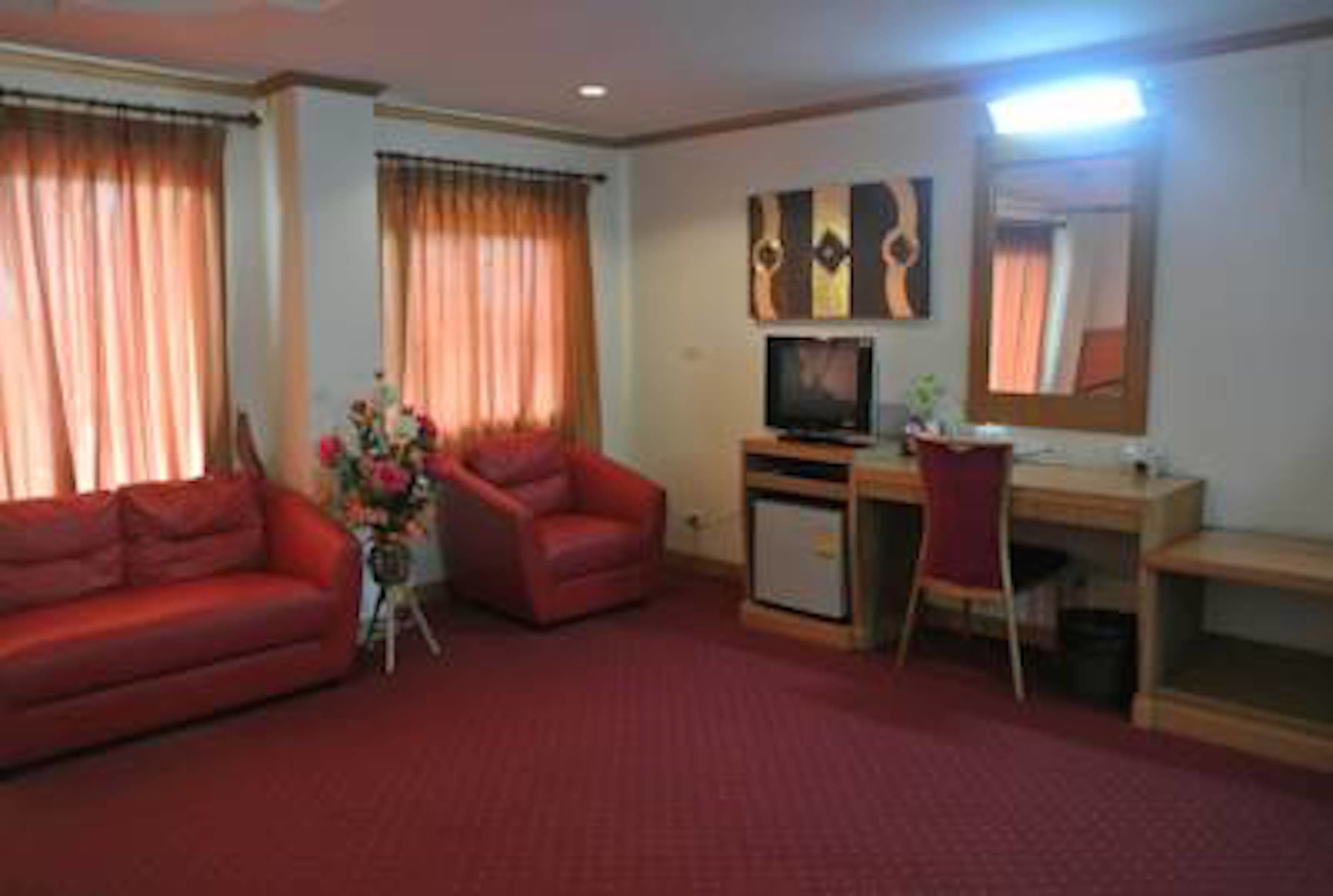 Ein Hotelzimmer mit einem roten Sofa, einem Schreibtisch mit Computer, einem Fernseher und einem Spiegel.