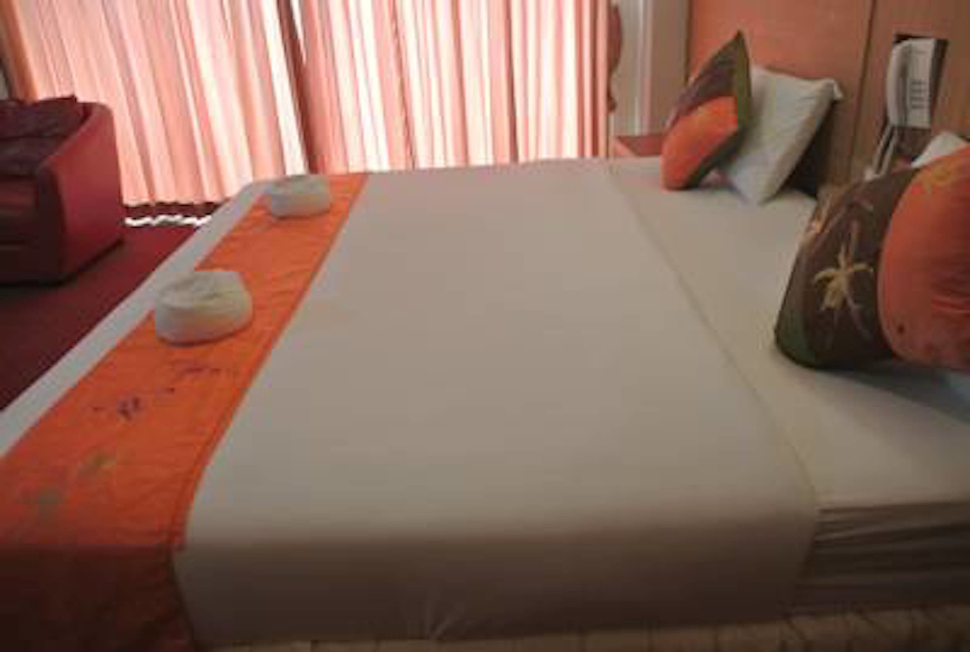 Una habitación de hotel con cama, almohadas, una silla roja y una ventana con cortinas.