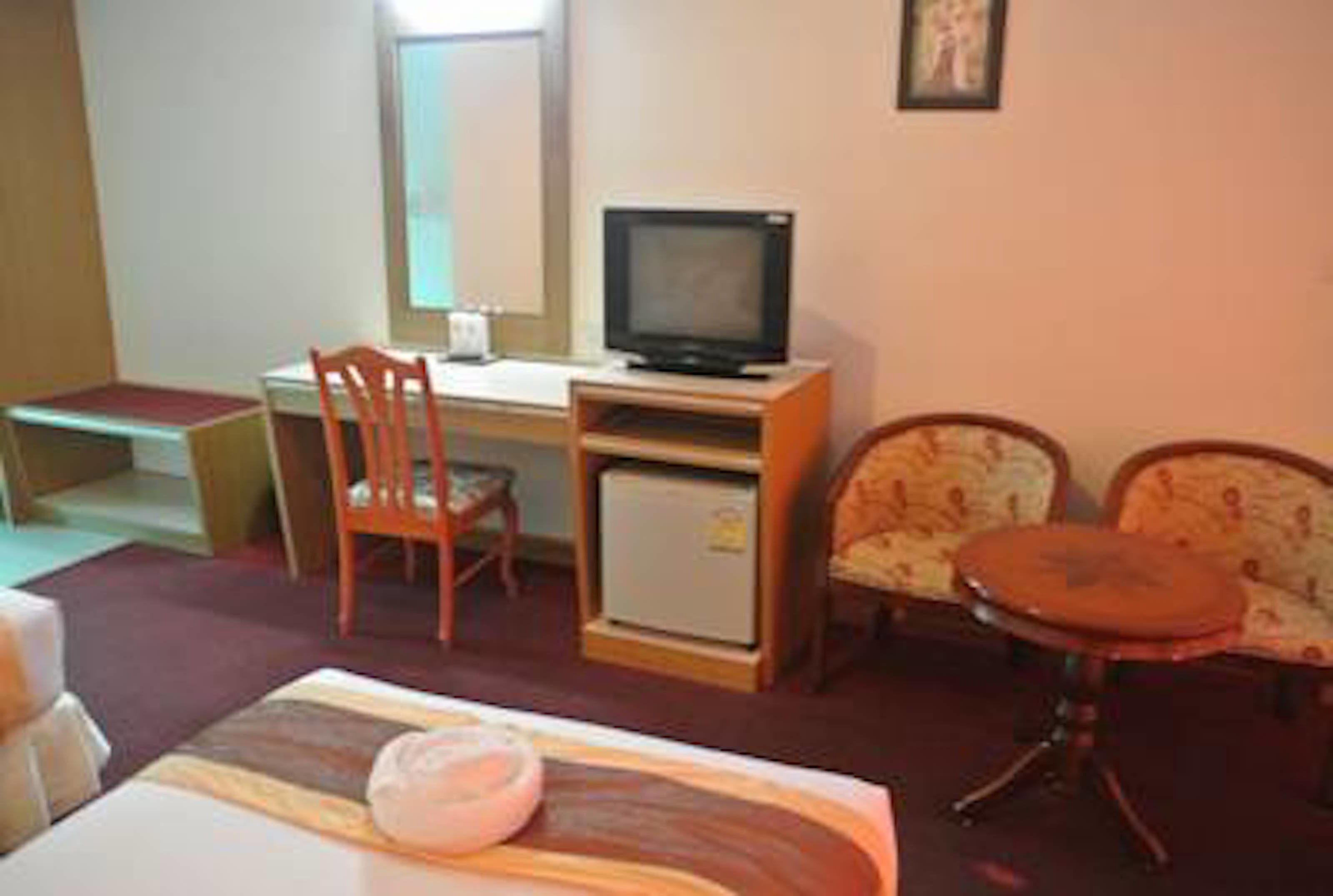 Habitació d'hotel amb llit, escriptori amb televisió, nevera petita, dues cadires i taula.