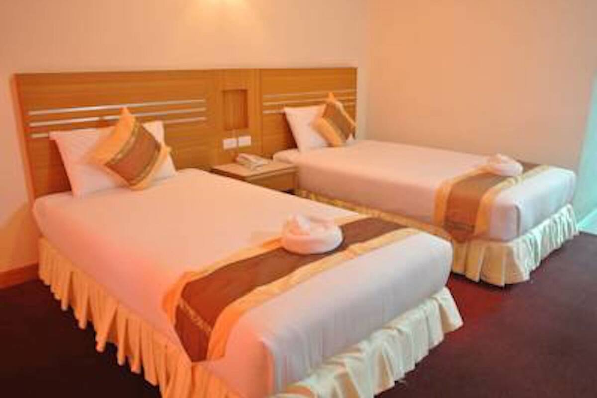 A hotel room with two beds, each with a wooden headboard, white bedding, and a decorative pillow.