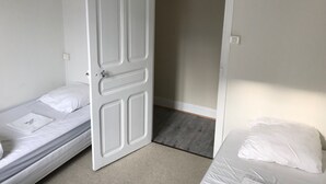 Et lille, enkelt værelse med to senge, en dør der fører til en gang, og en sort lampe over en af sengene.