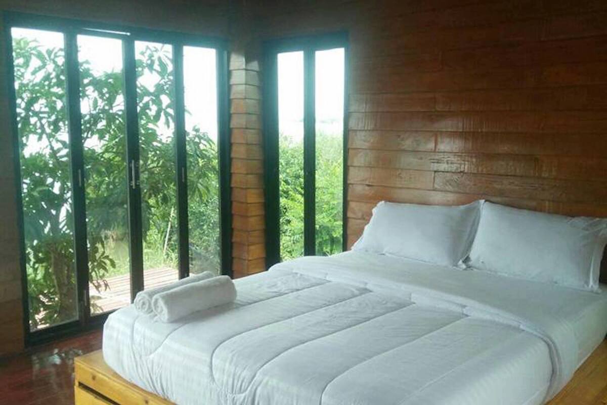 A large bed with white linens in a room with wooden walls and large windows.