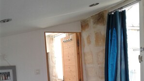 Une pièce avec une porte en bois, une petite table sur laquelle est posé un cadre photo, un tapis bleu et une fenêtre ornée de rideaux bleus.