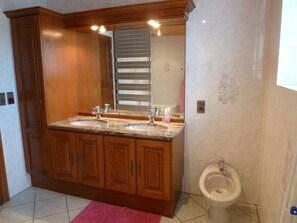 Une salle de bain avec des meubles en bois, un meuble-lavabo à deux vasques, des toilettes et un miroir.