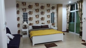 A bedroom with a bed, a nightstand, a lamp, a sofa, and a sliding glass door. - The Room Phatthalung (Phatthalung)