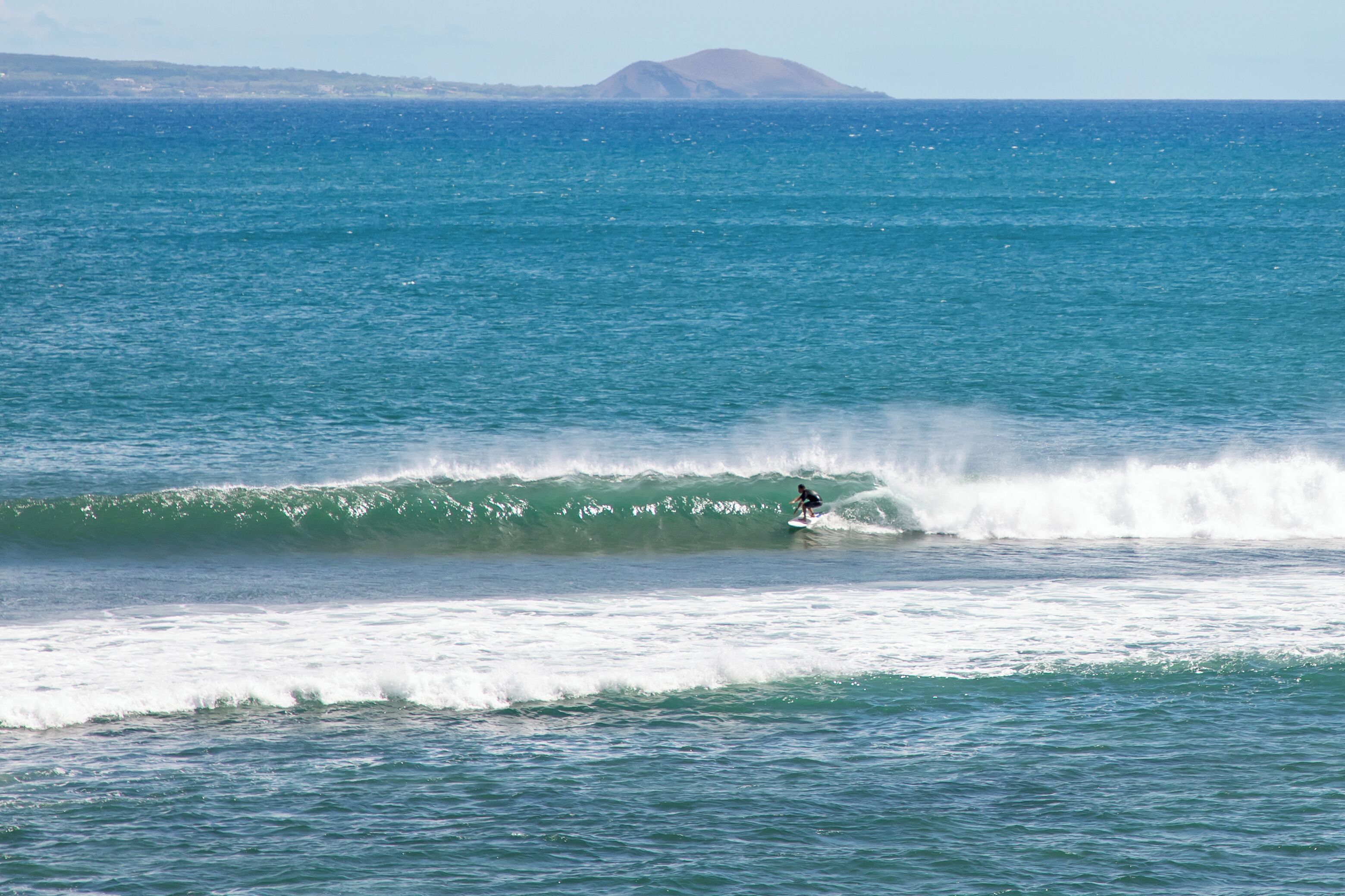Un surfeur chevauchant une vague dans l’océan, avec une montagne lointaine en arrière-plan.