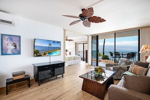 Un salón moderno con un televisor de pantalla plana grande, un ventilador de techo y un balcón con vistas al océano.