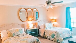A bedroom with two beds, a ceiling fan, and a large mirror.