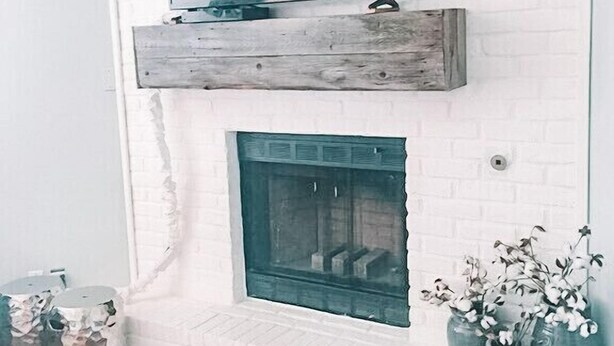 A modern fireplace with a TV mounted above it, a wooden mantel, and a small vase with flowers to the right.