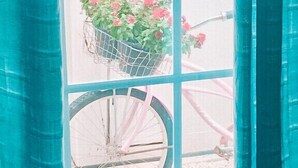 A window with a view of a pink bicycle with a basket of flowers.