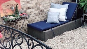 A wicker lounge chair with cushions, a decorative sign, and a small garden area with gravel.