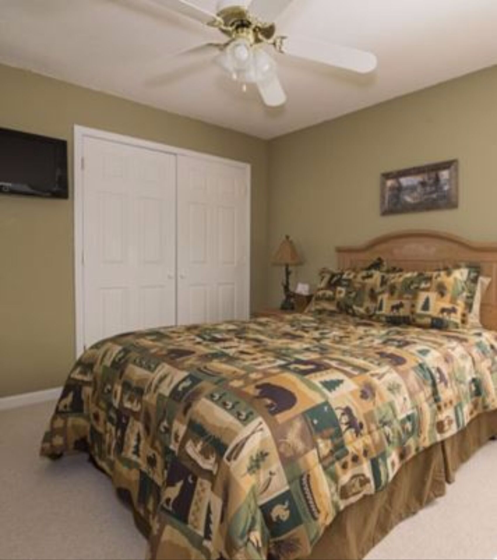 A bedroom with a bed, a ceiling fan, a white door, and a framed picture on the wall.