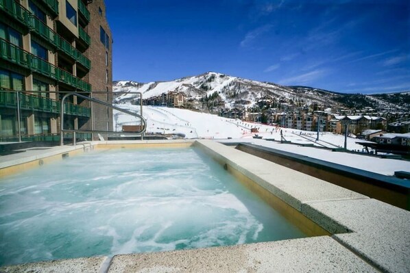 Un espace avec un bain à remous offrant une vue sur une montagne enneigée et des bâtiments en arrière-plan.