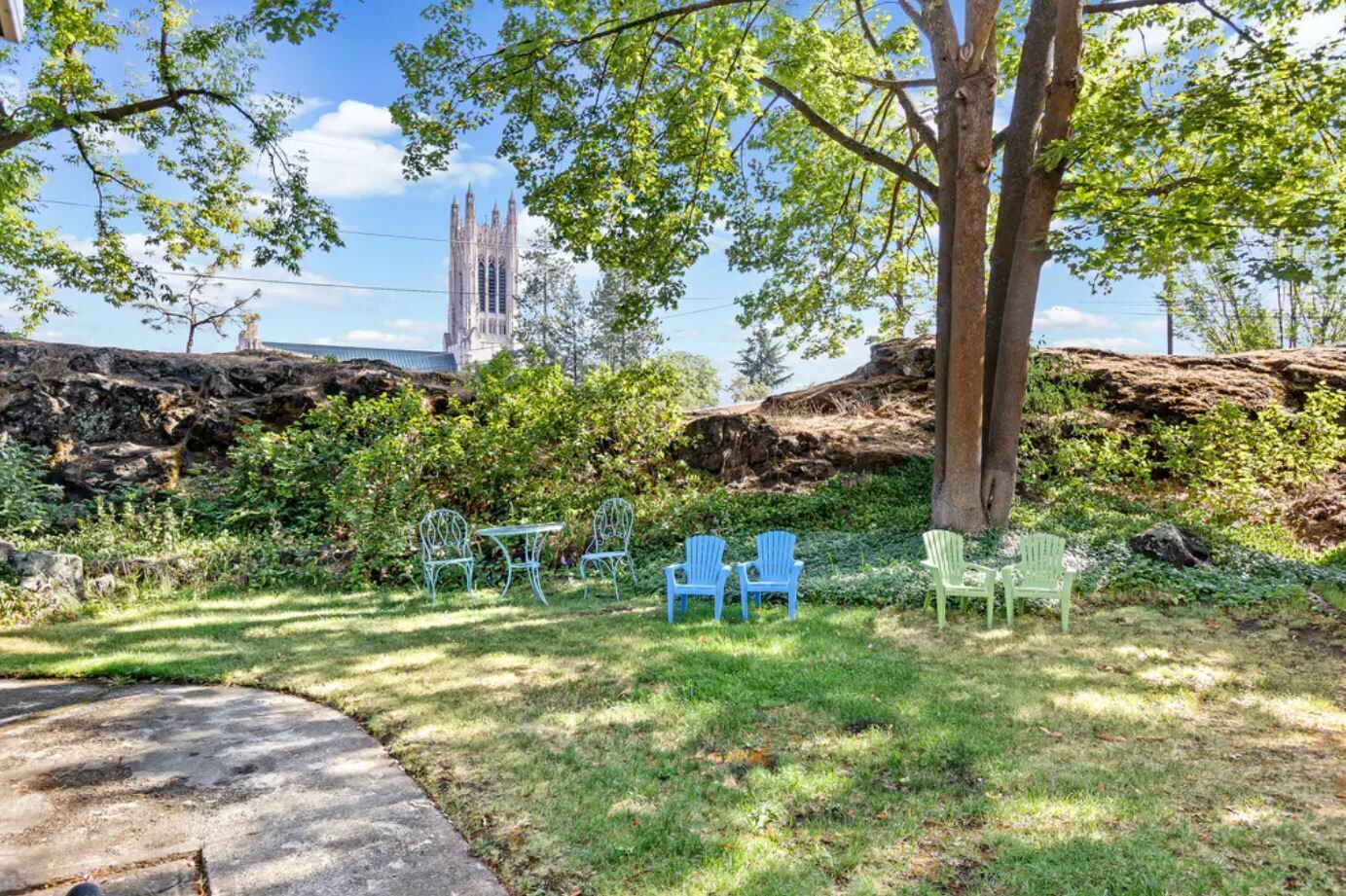 Un jardín con mobiliario exterior y un edificio histórico al fondo.