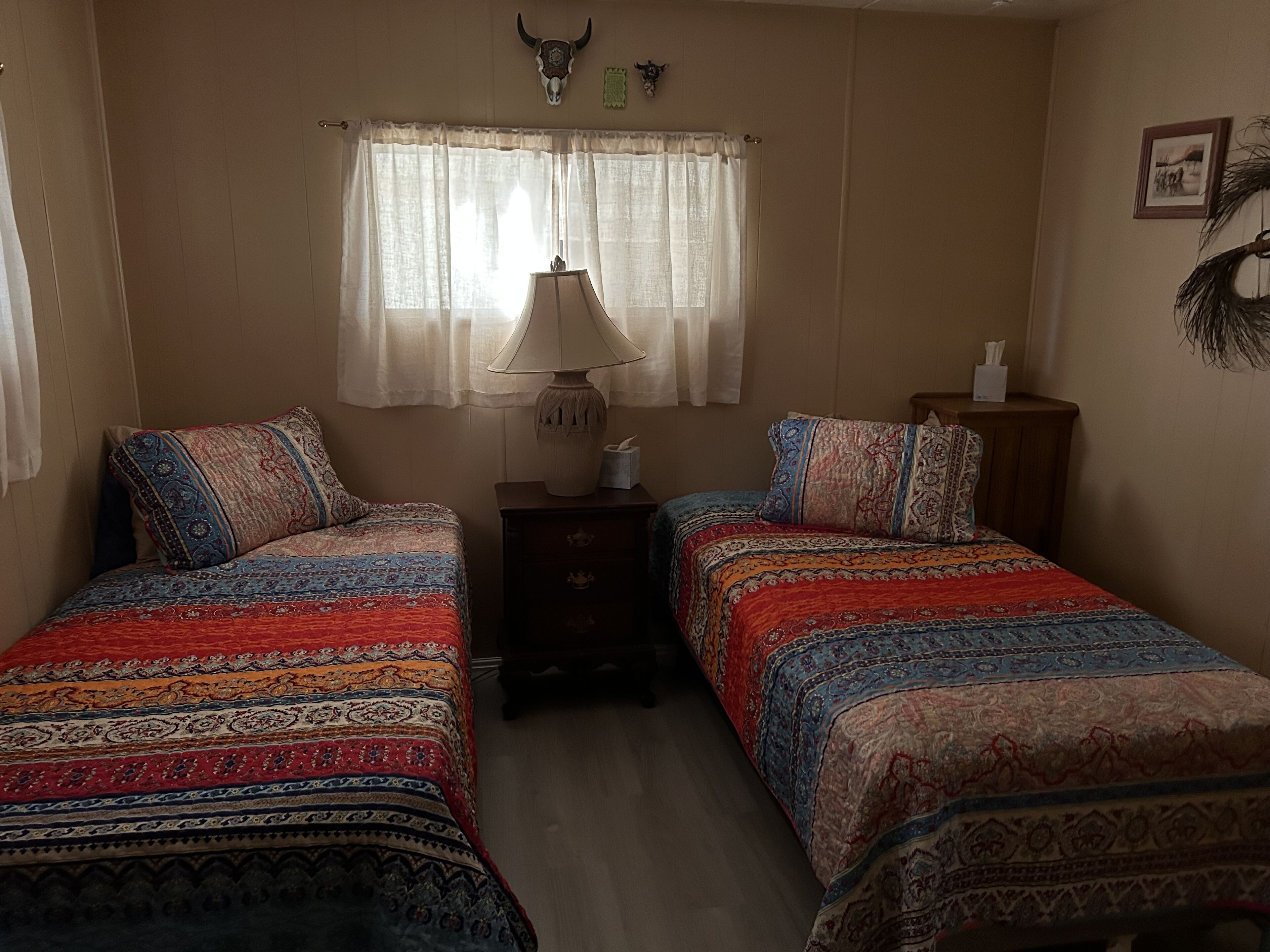 Une chambre avec deux lits, une table de chevet, une lampe et une fenêtre avec des rideaux.