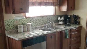 A kitchen with wooden cabinets, a dishwasher, a sink, and a window with curtains. - Family getaway, Pet Friendly, Snowbirds, Weekend Warriors,  Welcome  (Bullhead City)