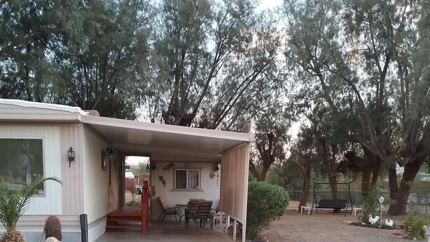 A mobile home with a covered porch, a dining area, and a small garden with trees and a swing set. - Family getaway, Pet Friendly, Snowbirds, Weekend Warriors,  Welcome  (Bullhead City)