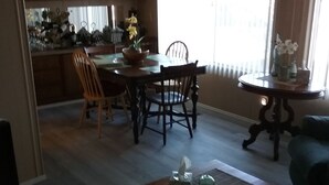 A dining area with a wooden table and chairs, a kitchen in the background, and a round side table with a vase. - Family getaway, Pet Friendly, Snowbirds, Weekend Warriors,  Welcome  (Bullhead City)