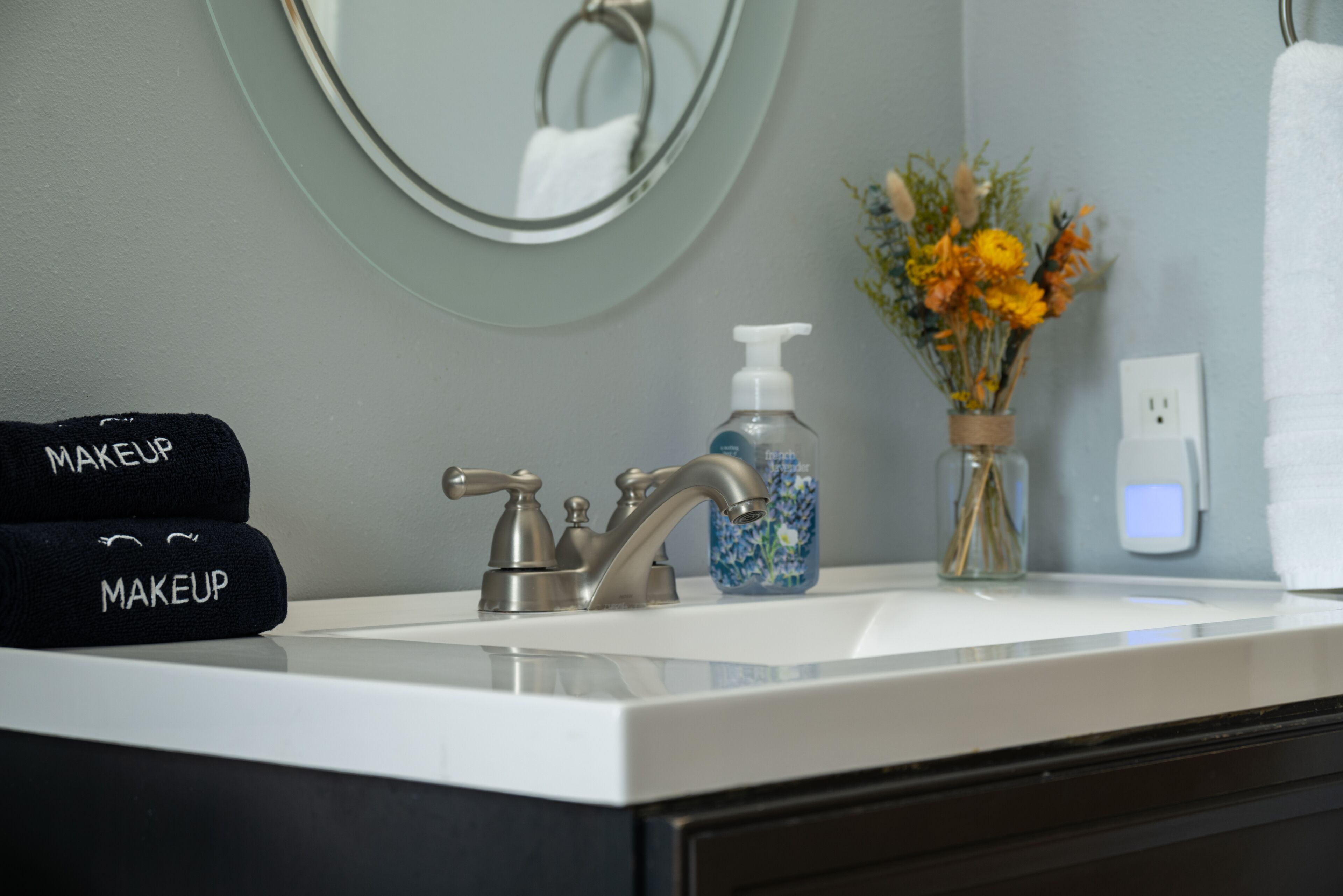 A bathroom sink with a modern faucet, a bottle of hand soap, and a vase with flowers.