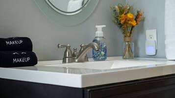A bathroom sink with a modern faucet, a bottle of hand soap, and a vase with flowers.