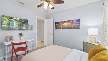 A bedroom with a bed, a desk, a chair, a TV, and artwork on the wall.