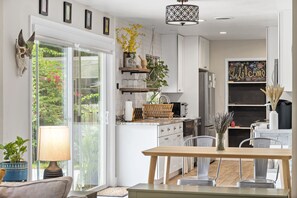 A modern kitchen with white cabinets, a wooden dining table, and a hanging light fixture. - A Home Where Eclectic Luxury Meets Affordability (Altamonte Springs)