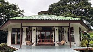 A house with a green roof, large windows, and two hanging chairs on the porch.