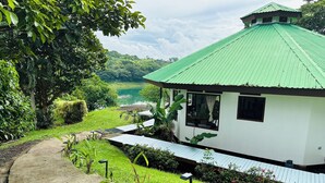A white building with a green roof, surrounded by lush greenery and a pathway leading to it.