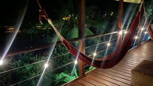 Un hamac suspendu entre des poutres en bois sur un balcon, illuminé de guirlandes lumineuses.