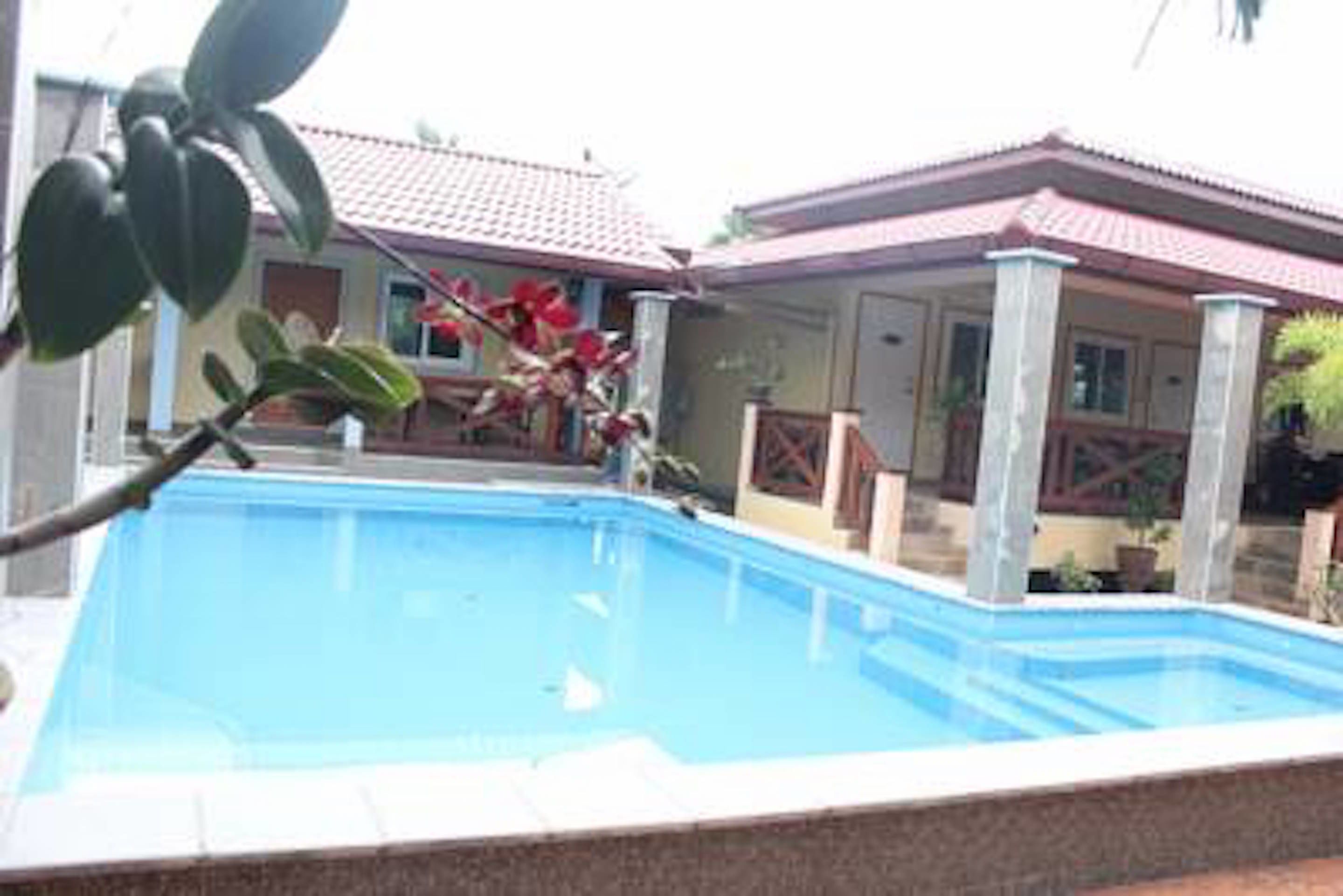 A swimming pool with a tiled deck, surrounded by a house with a red roof and white columns.
