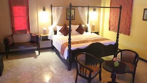 A four-poster bed with a canopy, two bedside tables with lamps, a small round table with a chair, and a bench with cushions. - Rimlay Park Resort (Phatthalung)