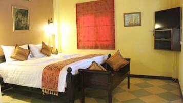 A hotel room with a bed, a bedside table, a chair, a red curtain, and a painting on the wall.