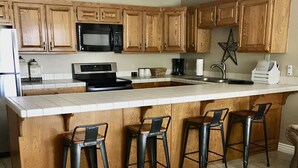 A kitchen with wooden cabinets, a central island with bar stools, a microwave, and a coffee maker. - Extra large one bedroom with access to the Las palmas Resort  pools. (Saint George)