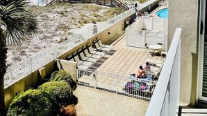 Ein Balkon mit Blick auf einen Strand, einen Pool und eine umzäunte Terrasse mit Stühlen und Tischen.