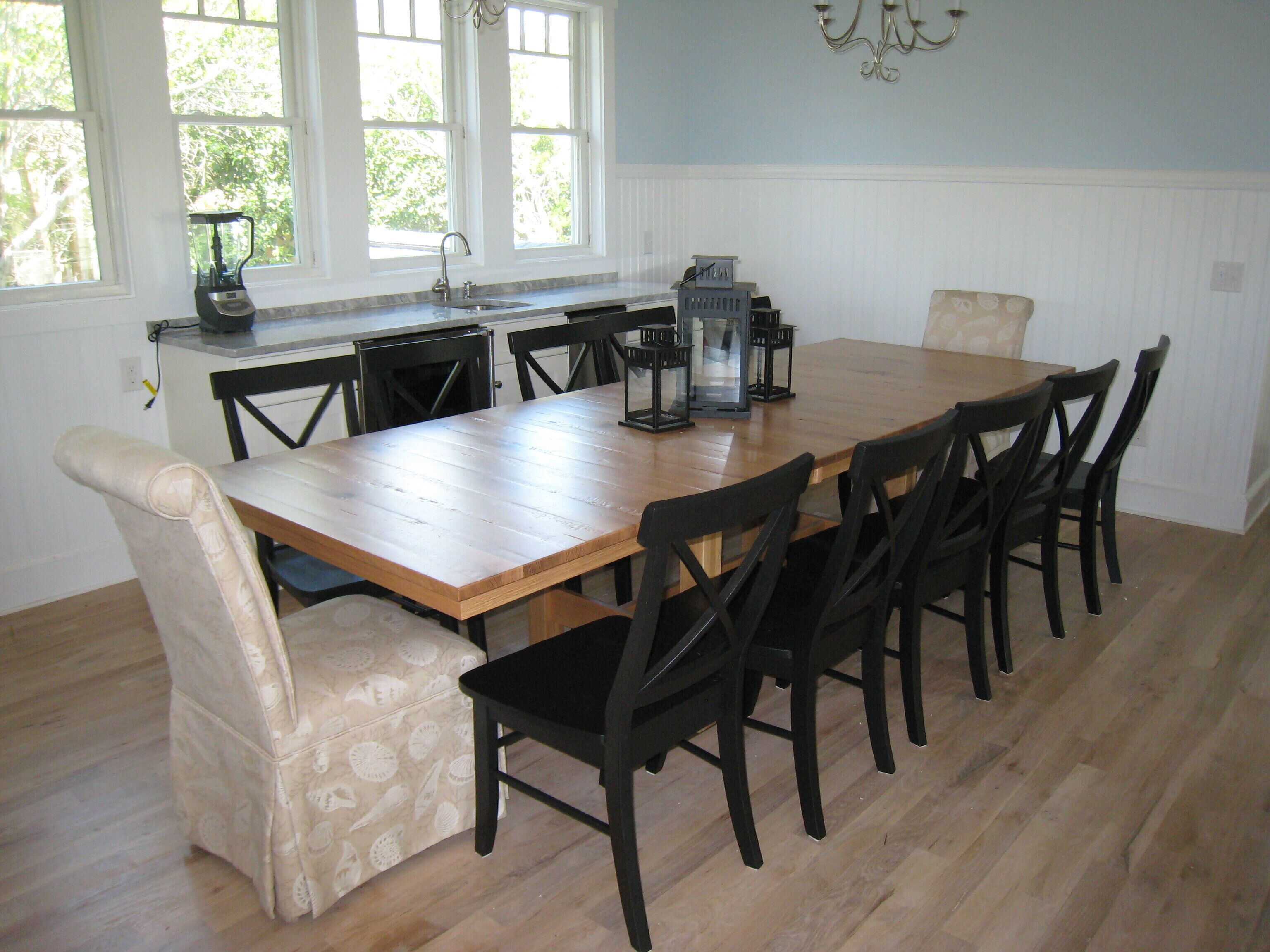 Un comedor con mesa de madera y sillas negras, una cocina con lavaplatos y estufa, y una araña.