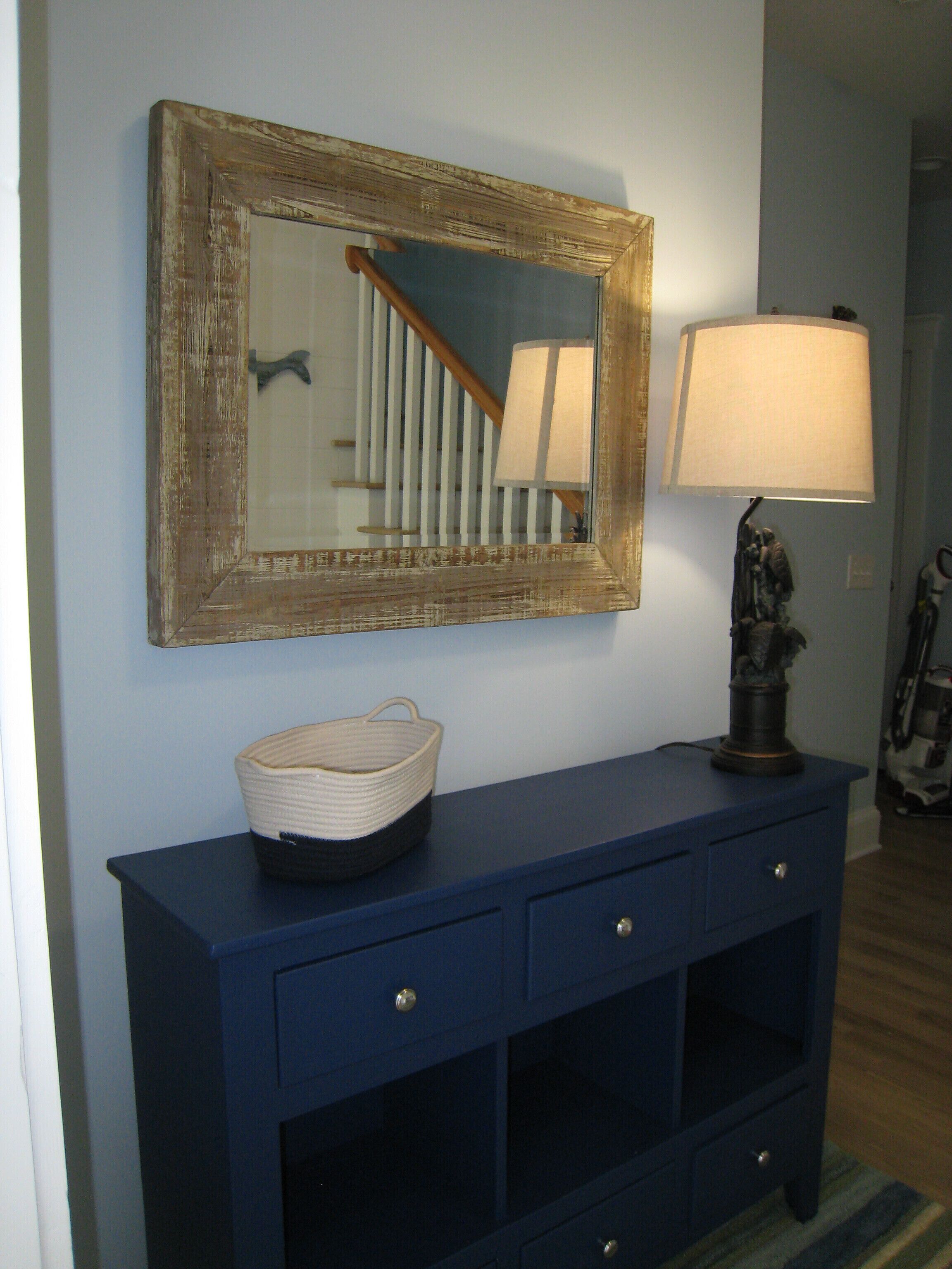 A dark blue console table with a woven basket, a lamp, and a mirror with a wooden frame.