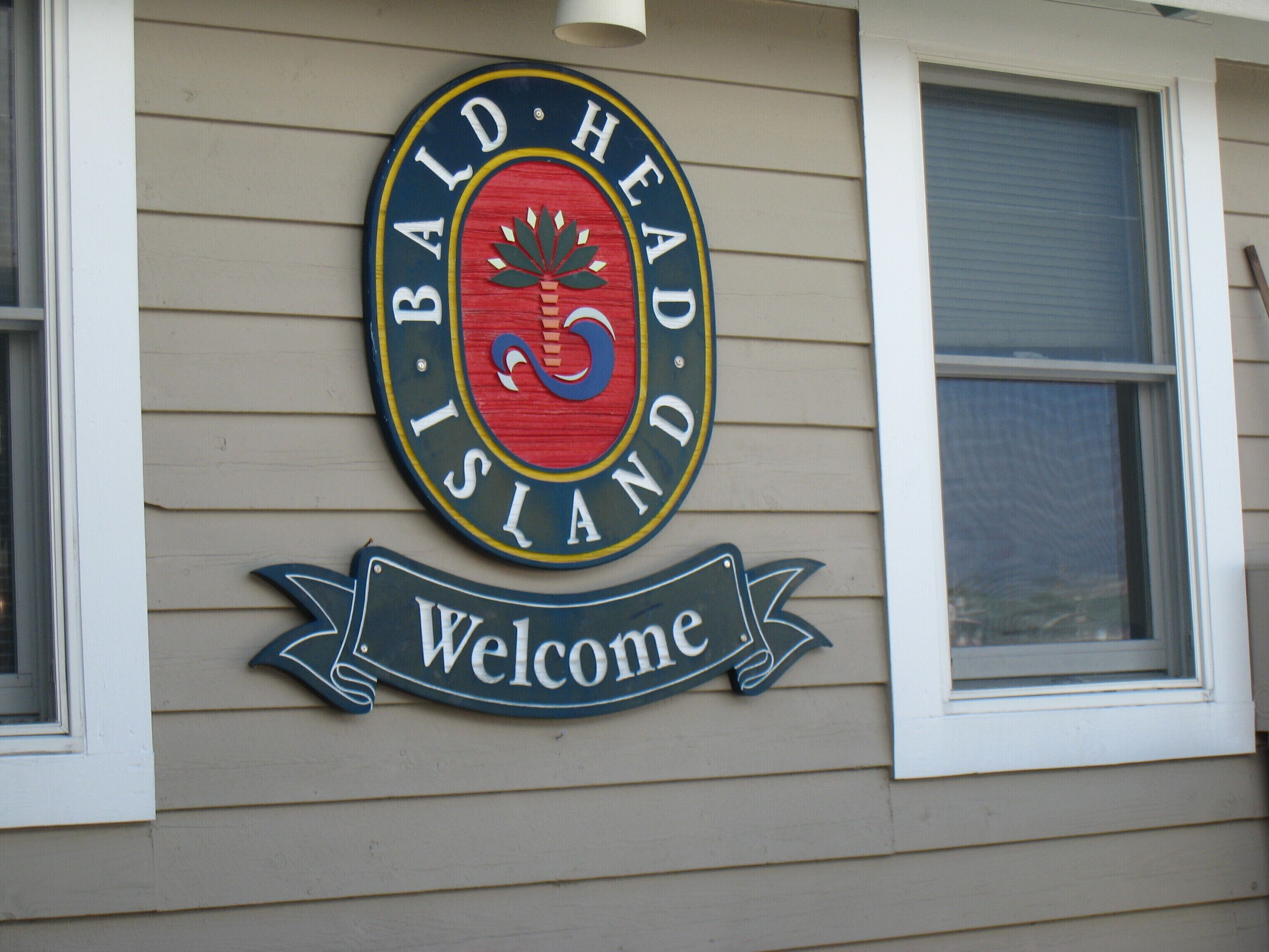 A circular sign with the text "BALD HEAD ISLAND" and "Welcome" on a building's exterior wall.