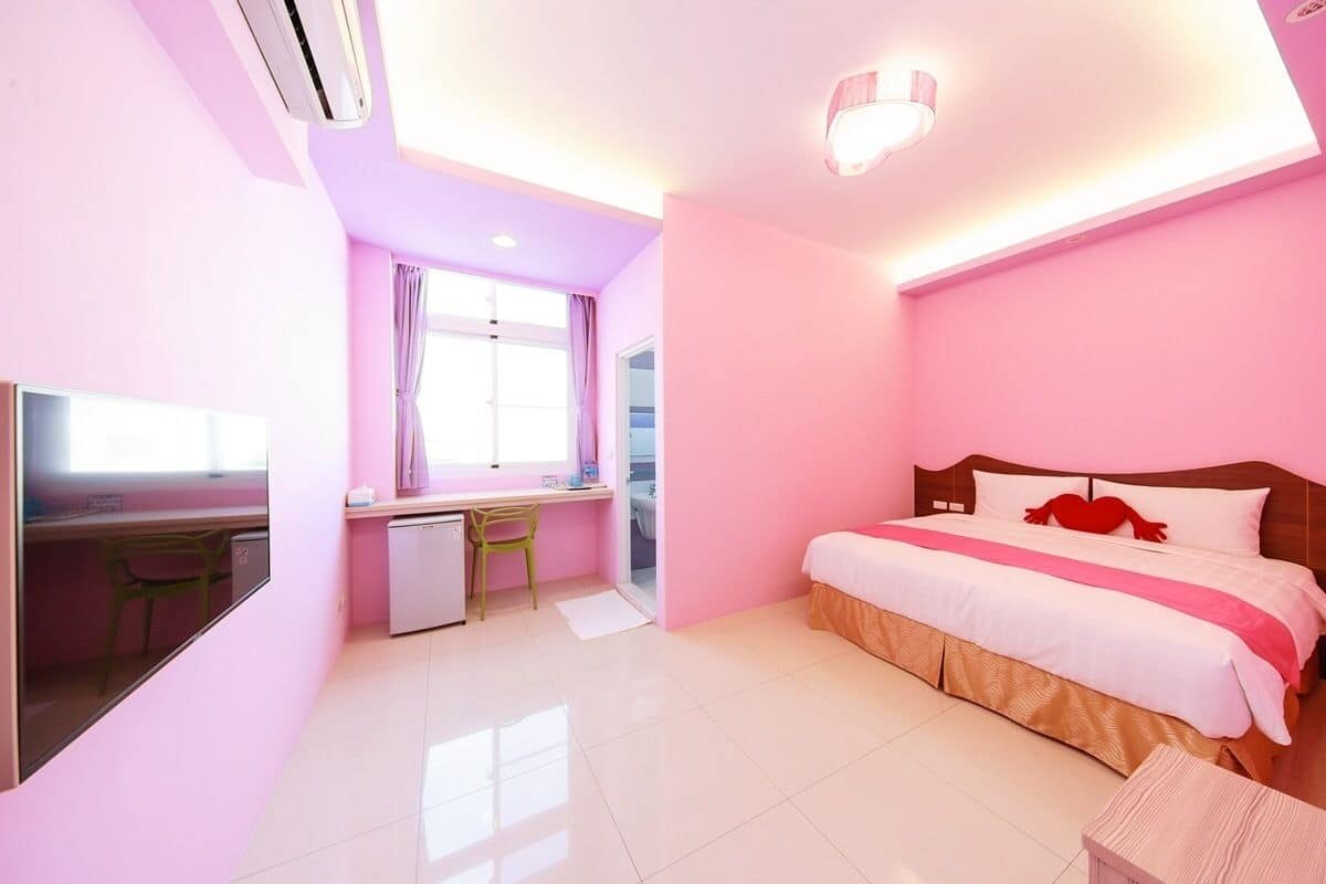 A pink-themed hotel room with a bed, desk, and chair.