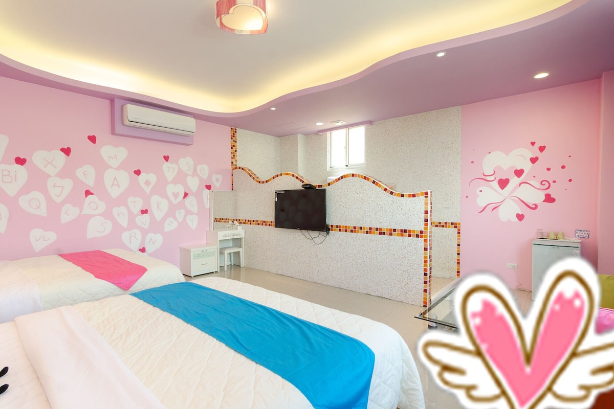 A bedroom with two beds, a TV mounted on the wall, and heart-themed decorations.