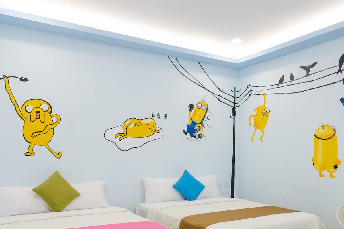 A bedroom with two beds, a nightstand, and a wall decorated with cartoon characters.