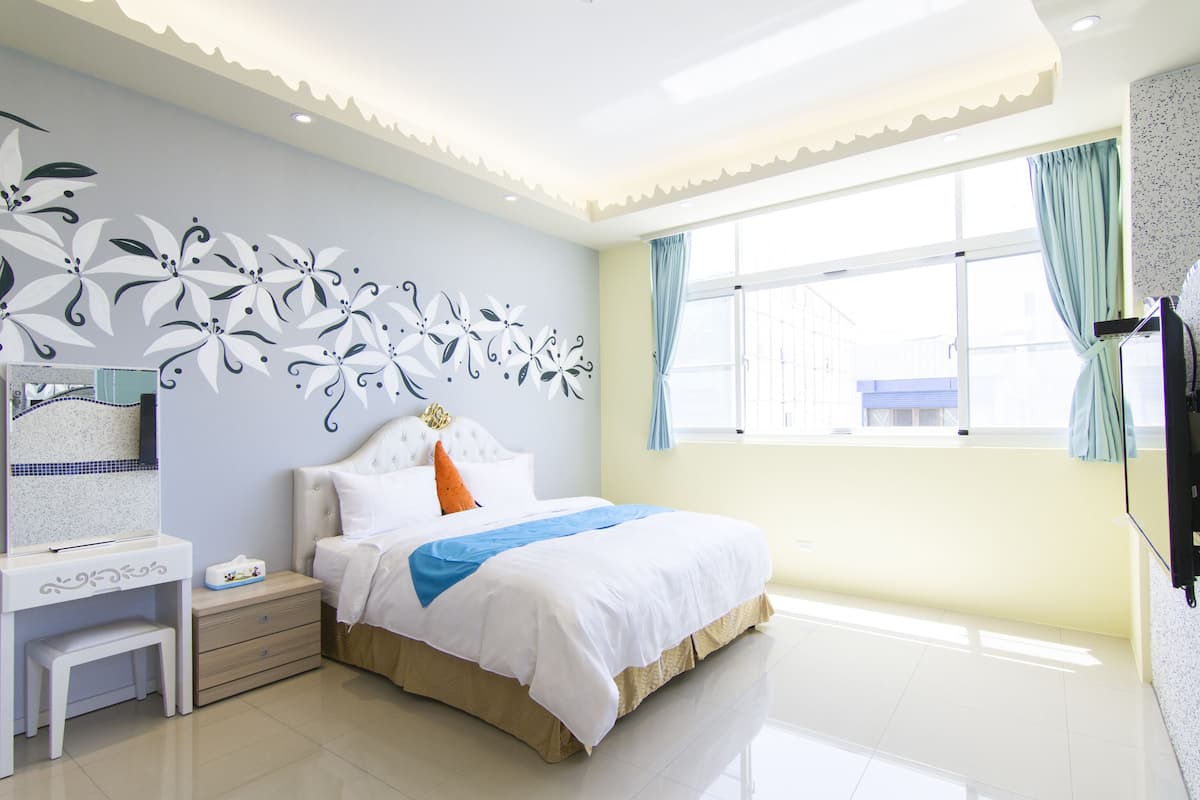 A bedroom with a bed, bedside table, and a window with curtains.