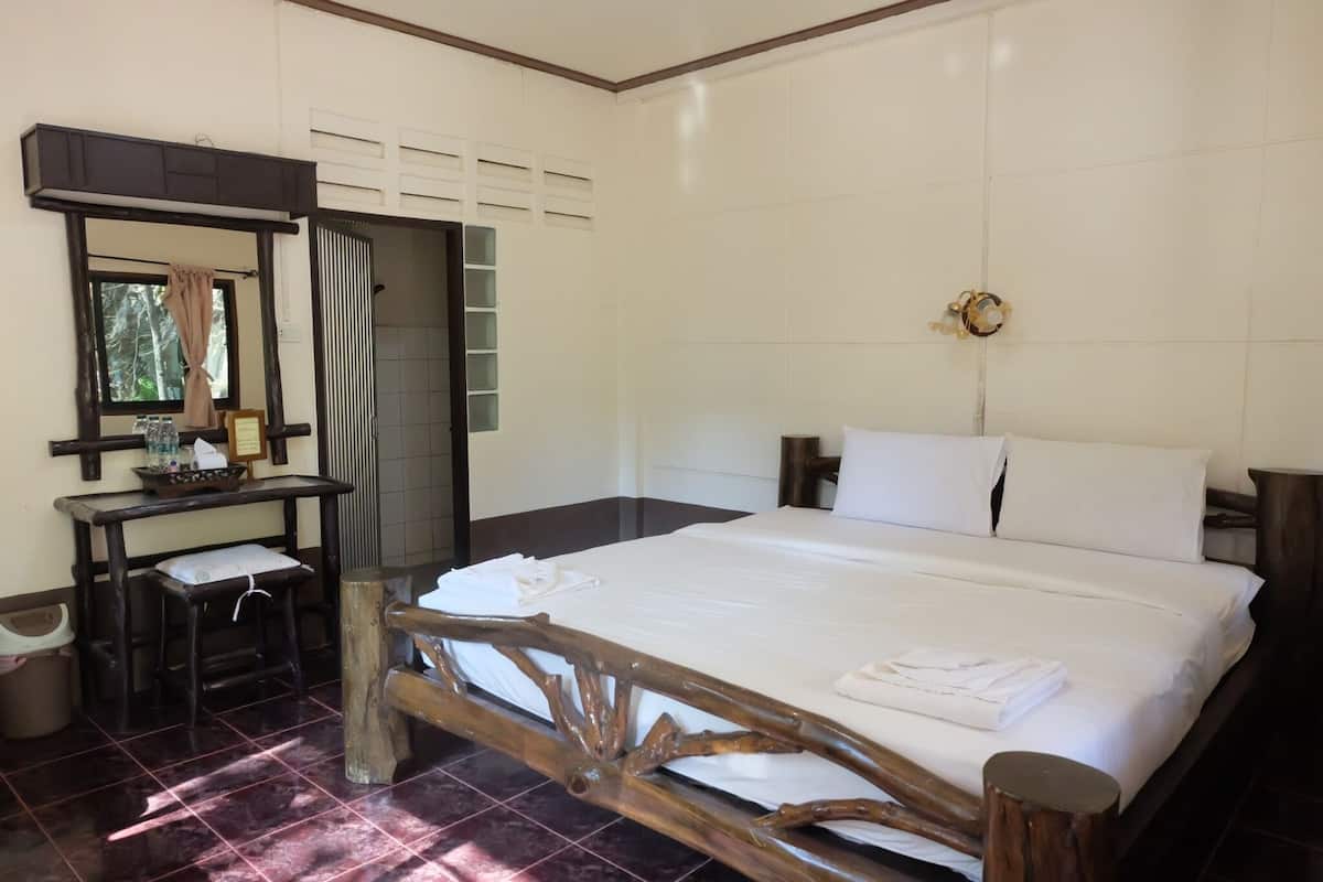 Habitación de hotel con estructura de cama de madera, un escritorio pequeño con una silla, un espejo y una ventana con cortinas.