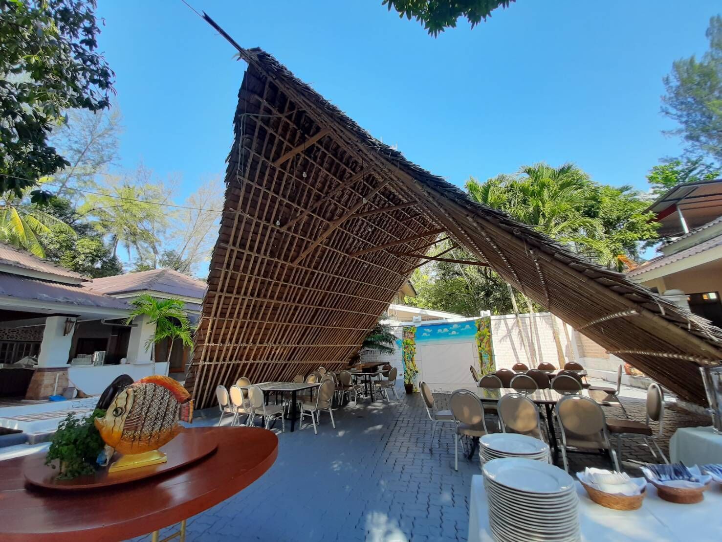 Un espacio de comedor al aire libre con sombrillas de bambú, mesas y sillas.