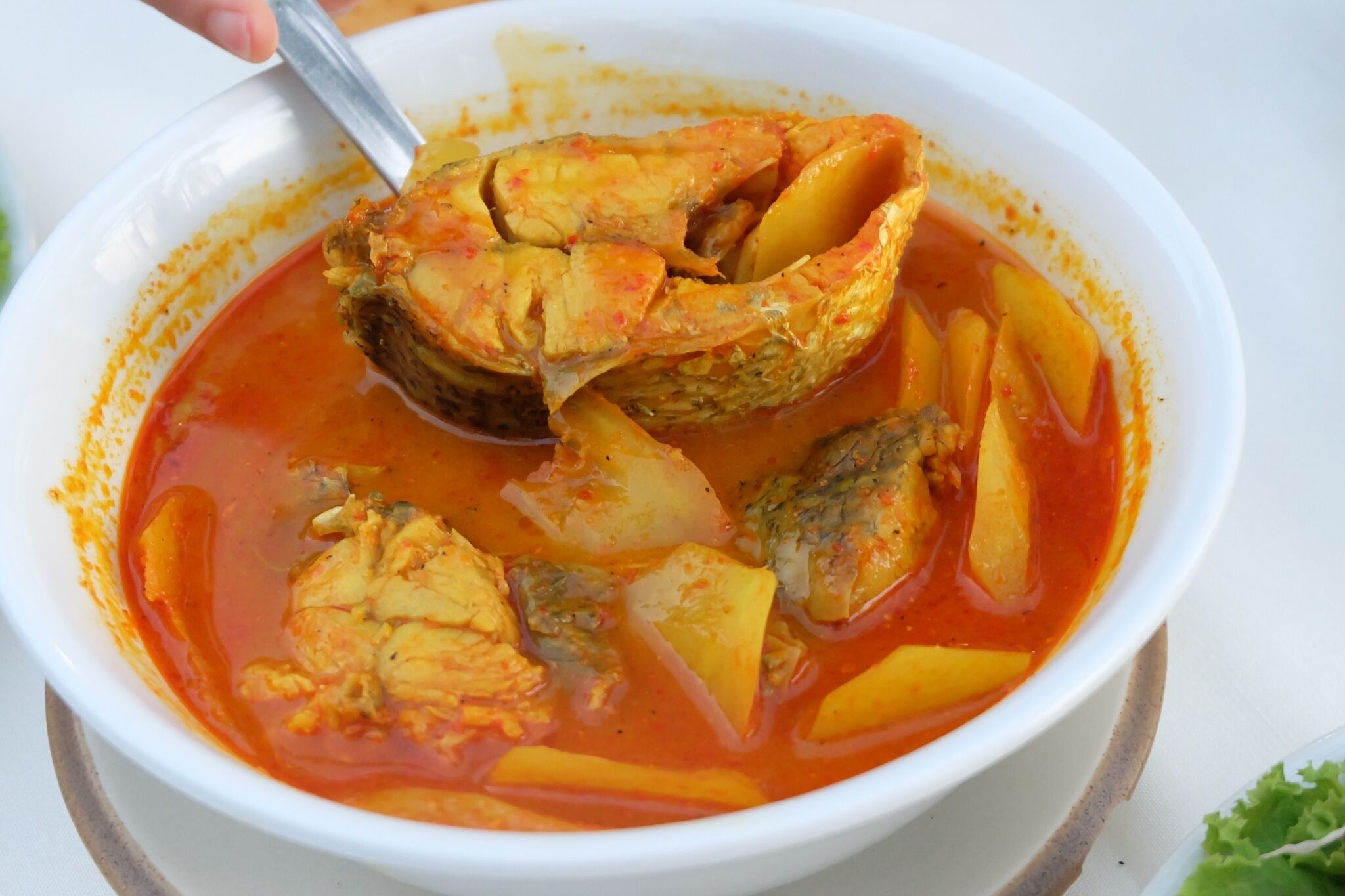 Un tazón de guiso de pescado con papas y una cuchara.