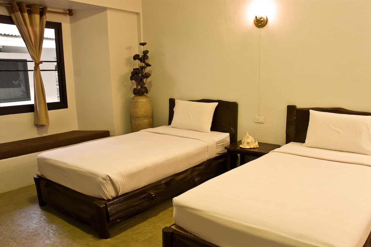 Una habitación de hotel con dos camas individuales, una mesita de noche con lámpara, un jarrón decorativo y una ventana con cortinas.