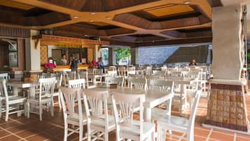 Un restaurant avec des tables et des chaises blanches, un pilier en pierre et un sol carrelé.