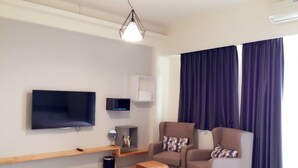 A modern living room with a flat-screen TV, two armchairs, a wooden coffee table, and a small side table with decorative items. - Happy Fat B&B (Taitung)