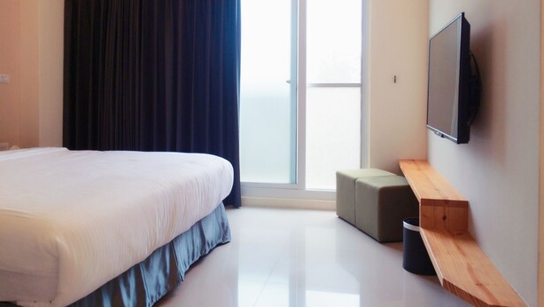 A modern hotel room with a large bed, a flat-screen TV mounted on the wall, a sliding glass door to the balcony, and a small wooden bench. - Happy Fat B&B (Taitung)